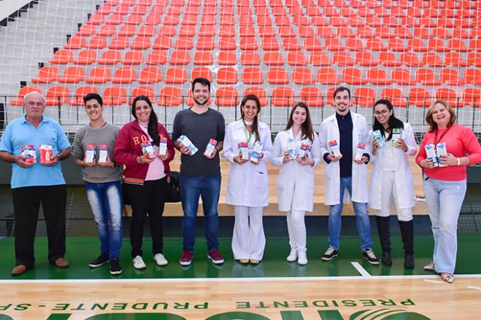 Entrega dos leites arrecadados: Docentes e alunos de Farmácia com representante da entidade (à esq.)
