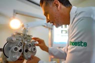 Profissional de saúde realizando um exame ocular em paciente usando equipamento especializado, vestindo jaleco com o logo da Unoeste.